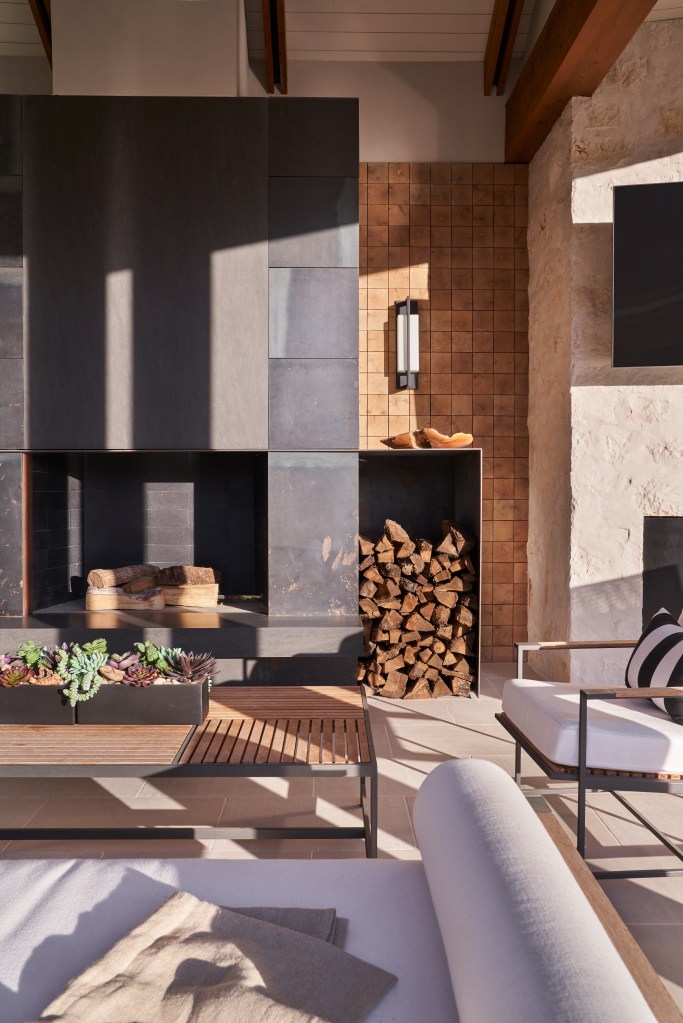 Covered outdoor living space with a blackened steel fireplace, end grain wood tile, limestone walls, and modern furnishings.